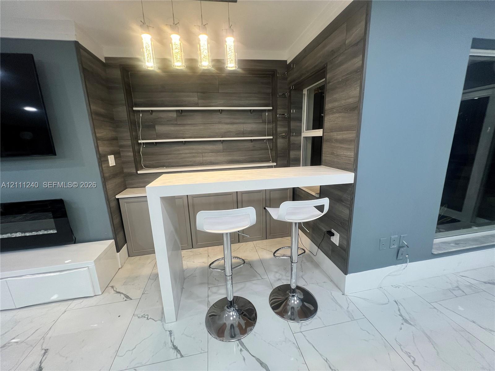 Built-in wet bar featuring a waterfall-edge countertop, grey cabinetry, integrated wood-finish wall paneling, open shelving, and multi-pendant lighting