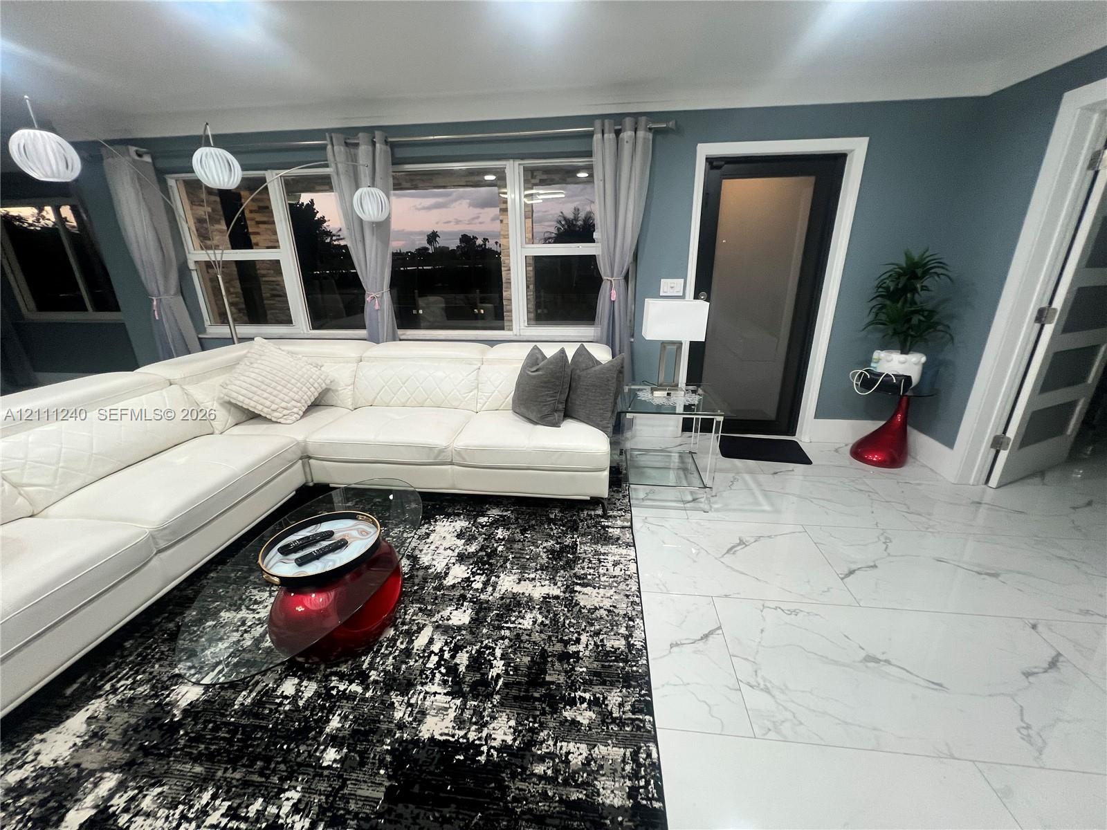 Large-format tile flooring with a polished finish, expansive windows with grid detailing, glass-panel exterior door, and multi-pendant overhead lighting