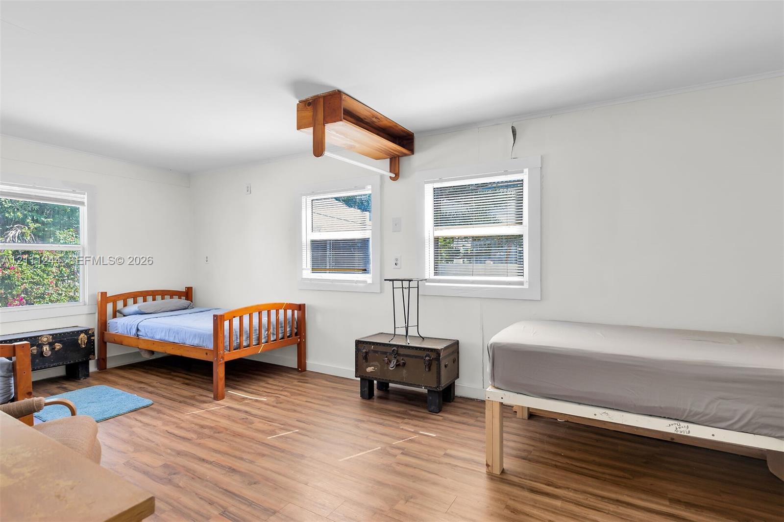 Interior space featuring wood-finish flooring, white walls, and multiple double-hung windows, highlighted by a built-in overhead wooden storage shelf with a hanging rod