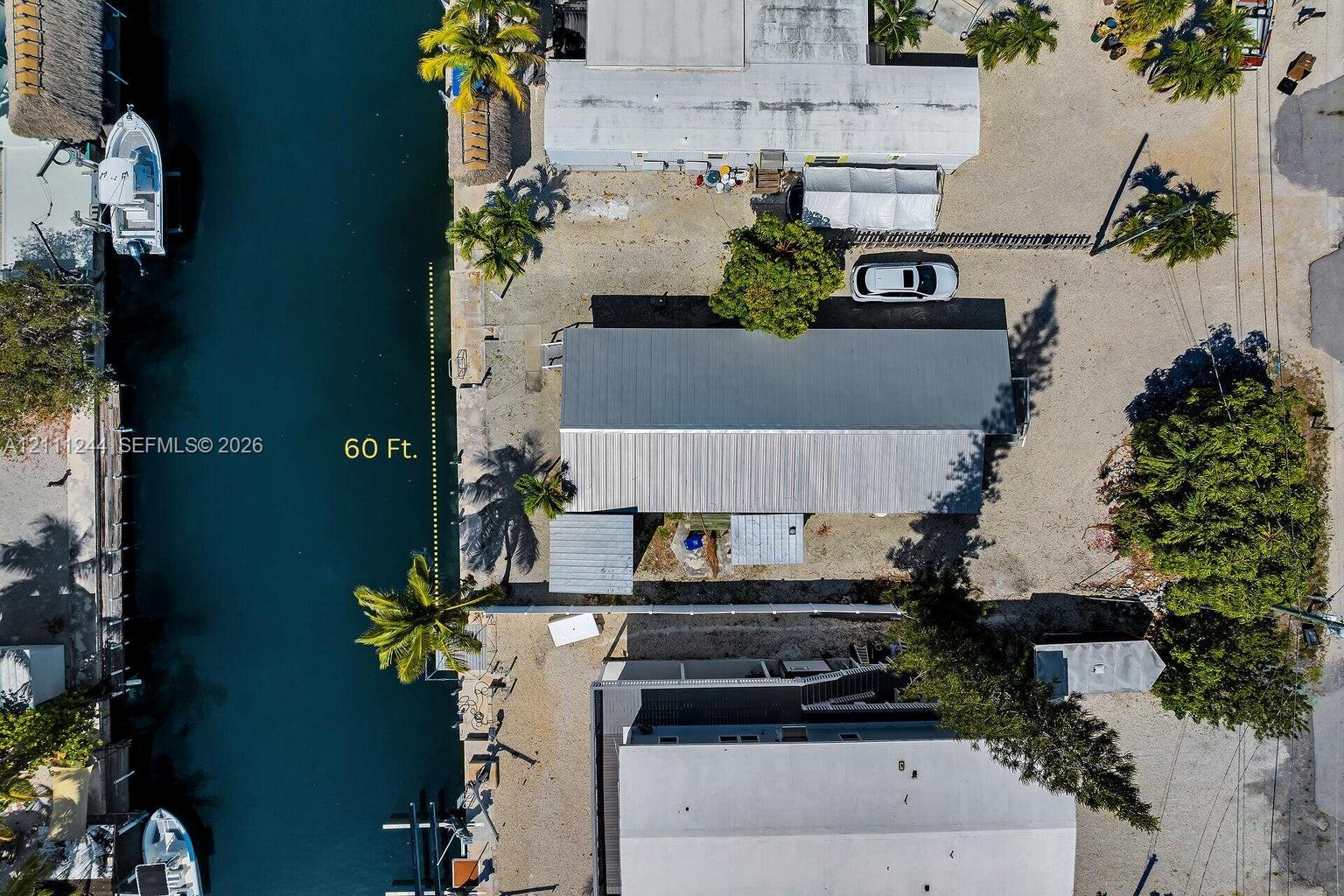 Aerial perspective of a waterfront property featuring 60 feet of canal frontage, a metal roof structure, and mature palms
