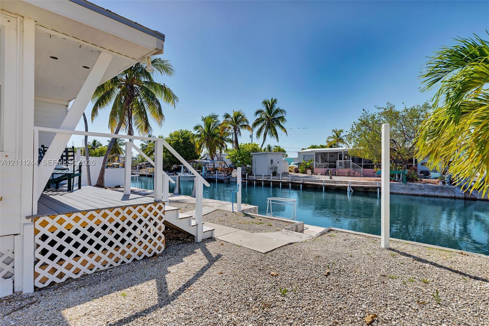 Waterfront property featuring a canal-side deck, white lattice skirting, stairs with a wooden railing, and a gravel yard