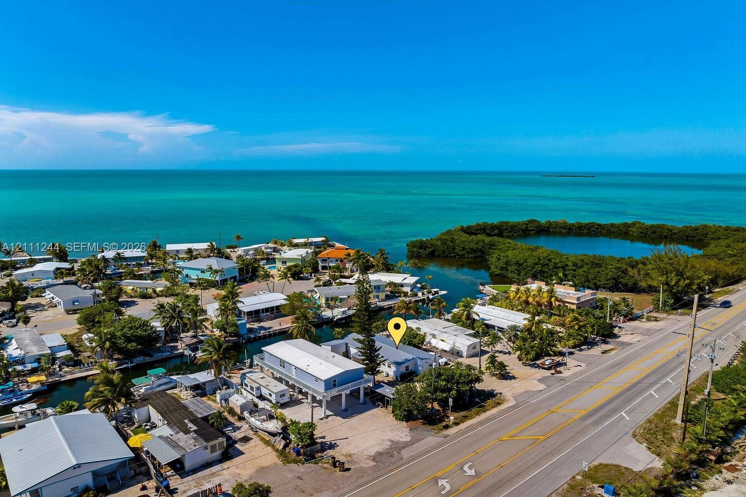 Aerial perspective of a coastal property featuring waterfront access, elevated structural design, gravel lot, and proximity to open water