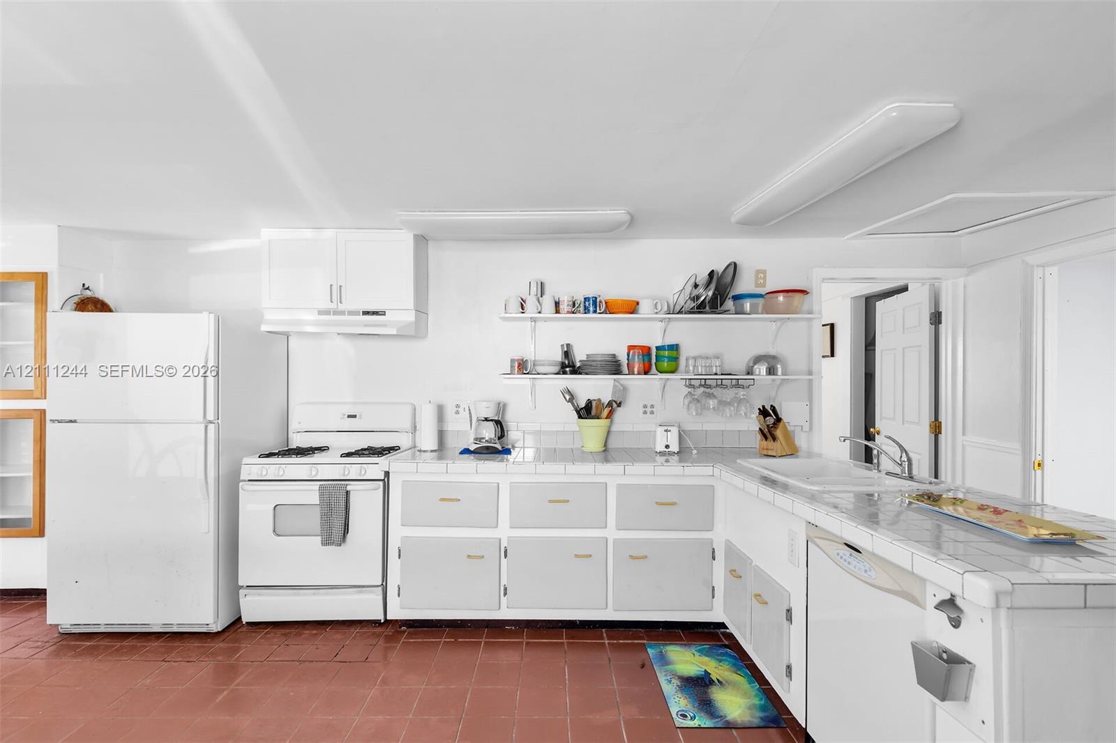 Kitchen featuring white cabinetry, tile countertops, integrated white appliances, open shelving, and tiled flooring