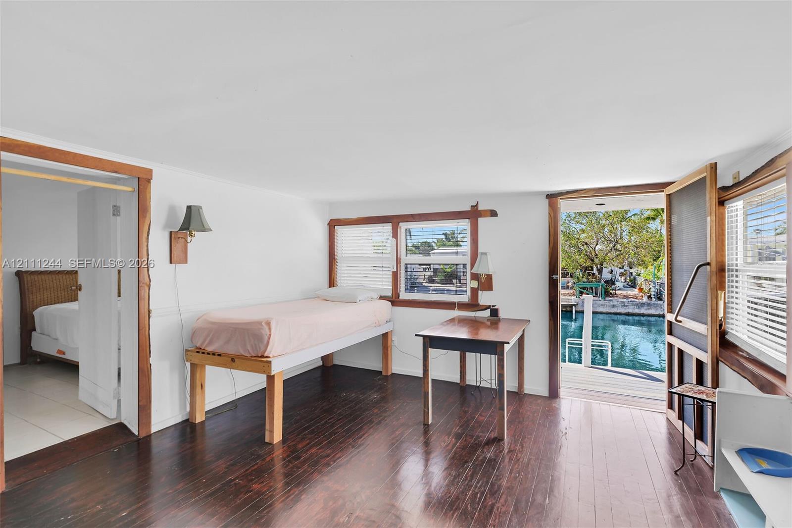 Interior featuring dark-stained wood-finish flooring, natural wood door and window trim, dual wall-mounted light fixtures, and a screen door opening to a private dock with canal access