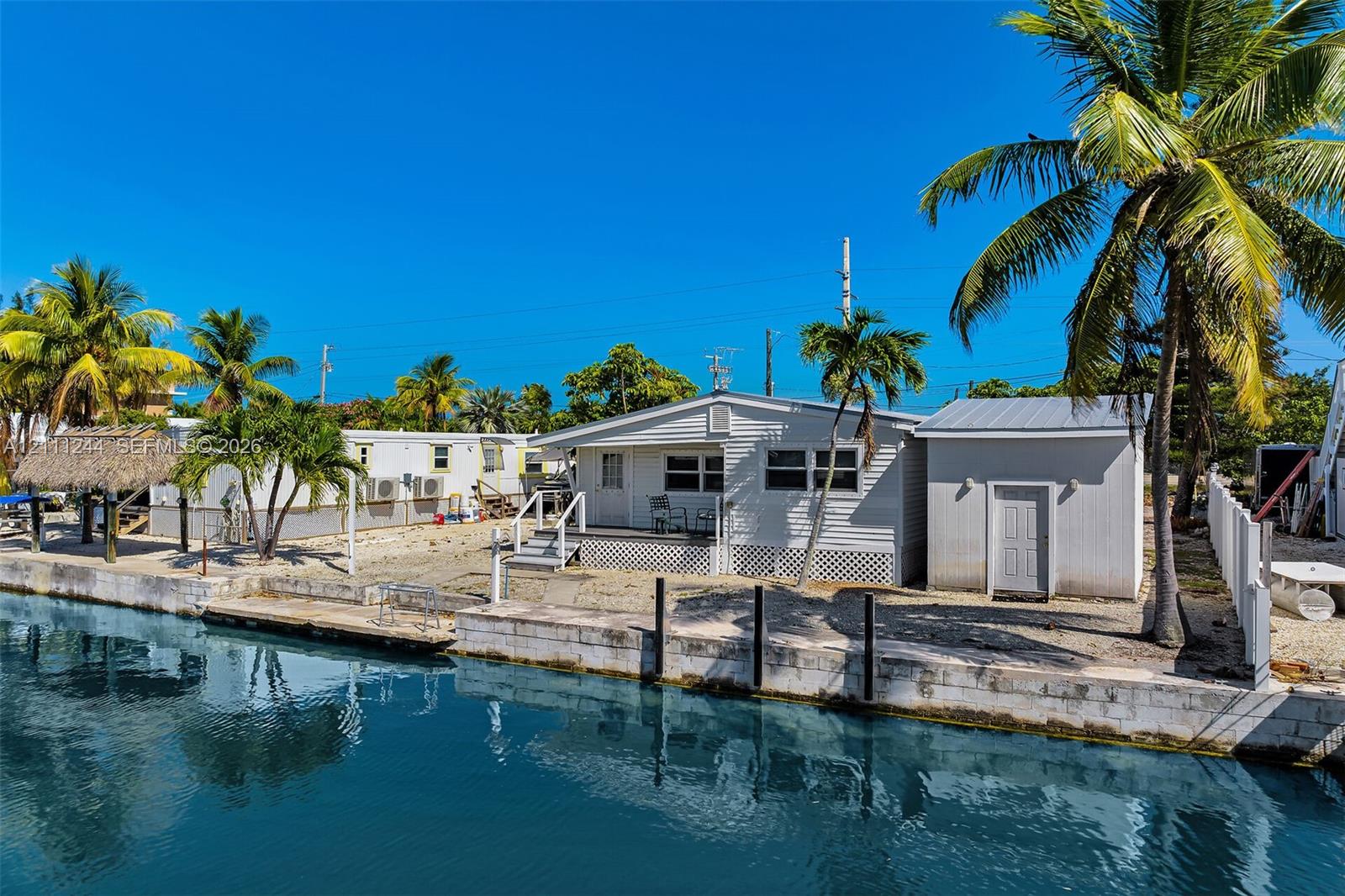 Waterfront property featuring a concrete seawall, detached storage structure, metal roof, and palm tree landscaping