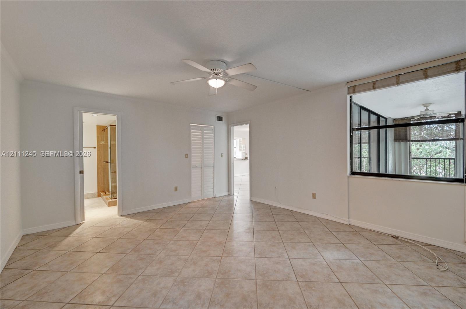Room featuring large-format diagonal tile flooring, ceiling fan with integrated light fixture, louvered closet doors, and a multi-pane window with exterior greenery