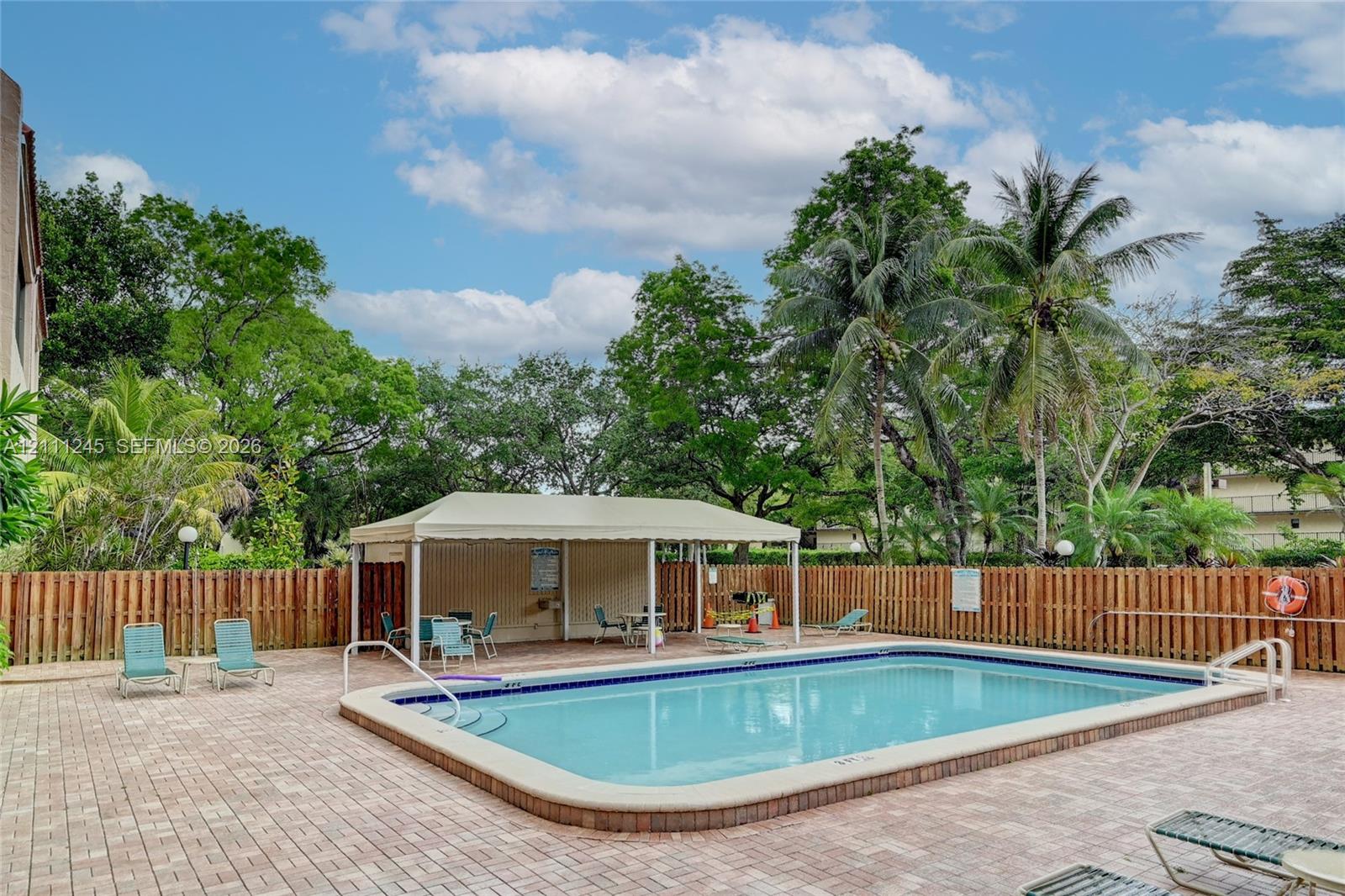 In-ground swimming pool with surrounding brick-paver decking, covered pavilion, and privacy fencing