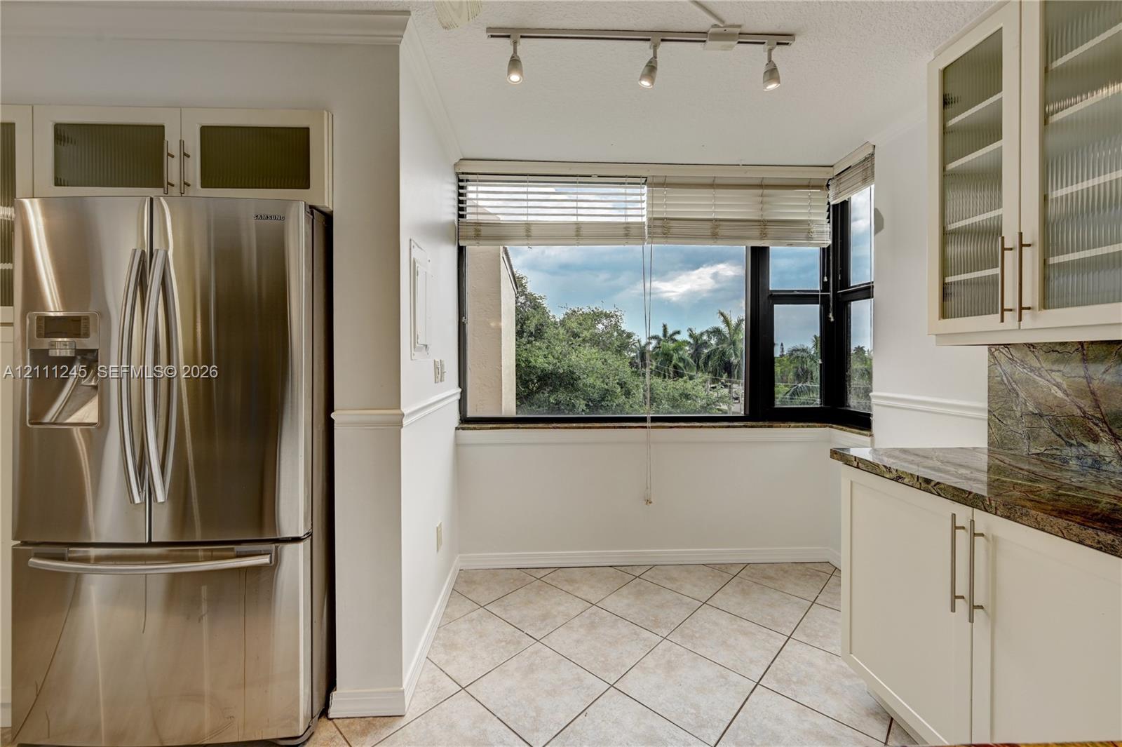 Kitchen featuring stainless steel French door refrigerator, white cabinetry with glass-front uppers, stone-finish countertops, tile flooring, and track lighting