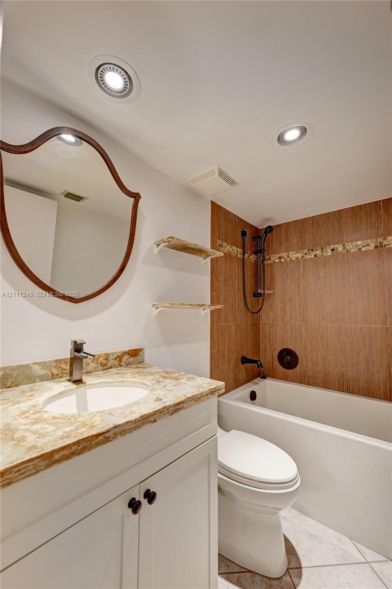 Bathroom featuring a white vanity with a neutral stone countertop, recessed ceiling lighting, wall-mounted open shelving, and a shower-tub combination with wood-finish tile surround and decorative mosaic accent