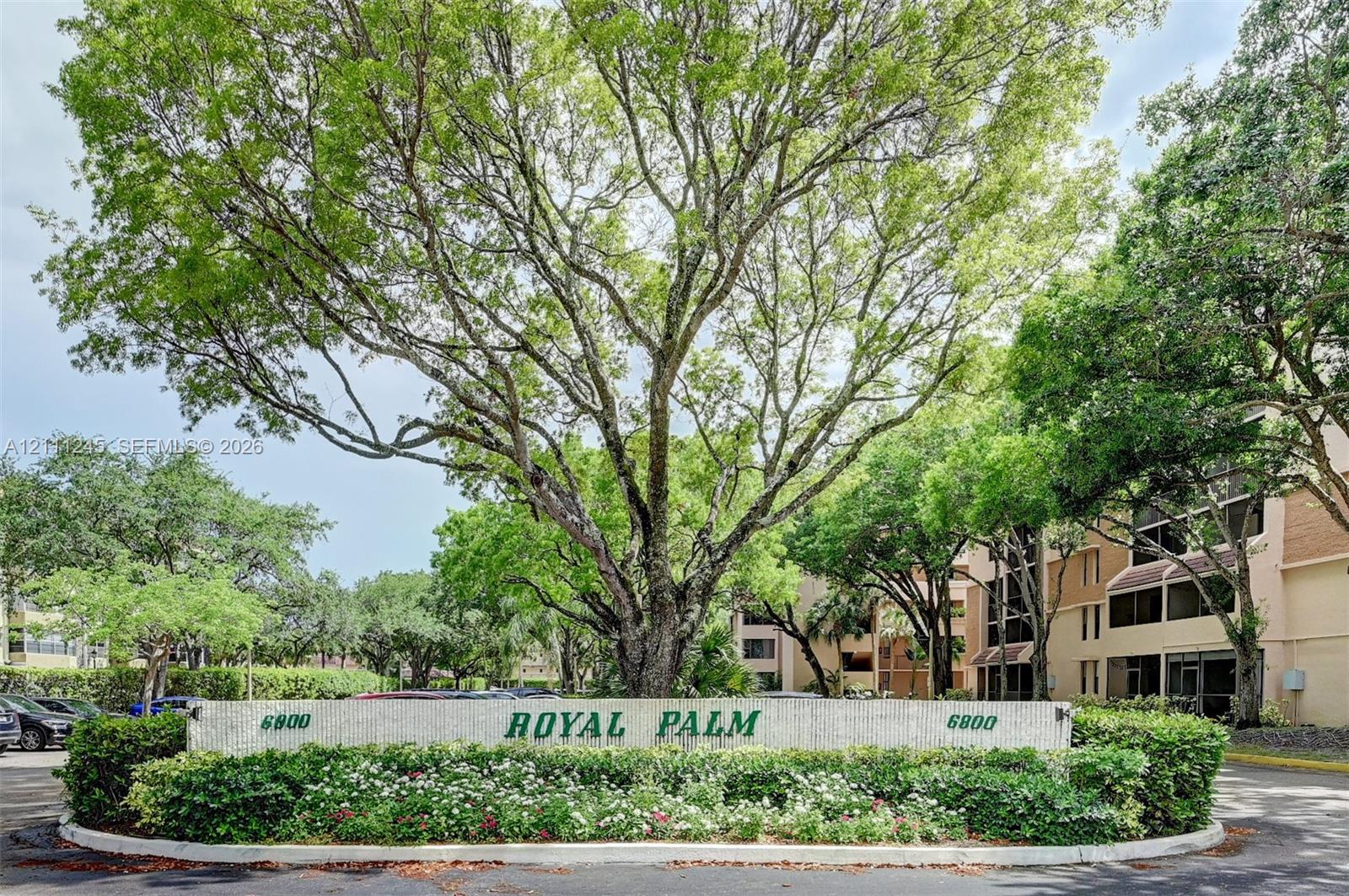 Monument entrance sign with stone-finish base, integrated landscaping, and large mature shade trees