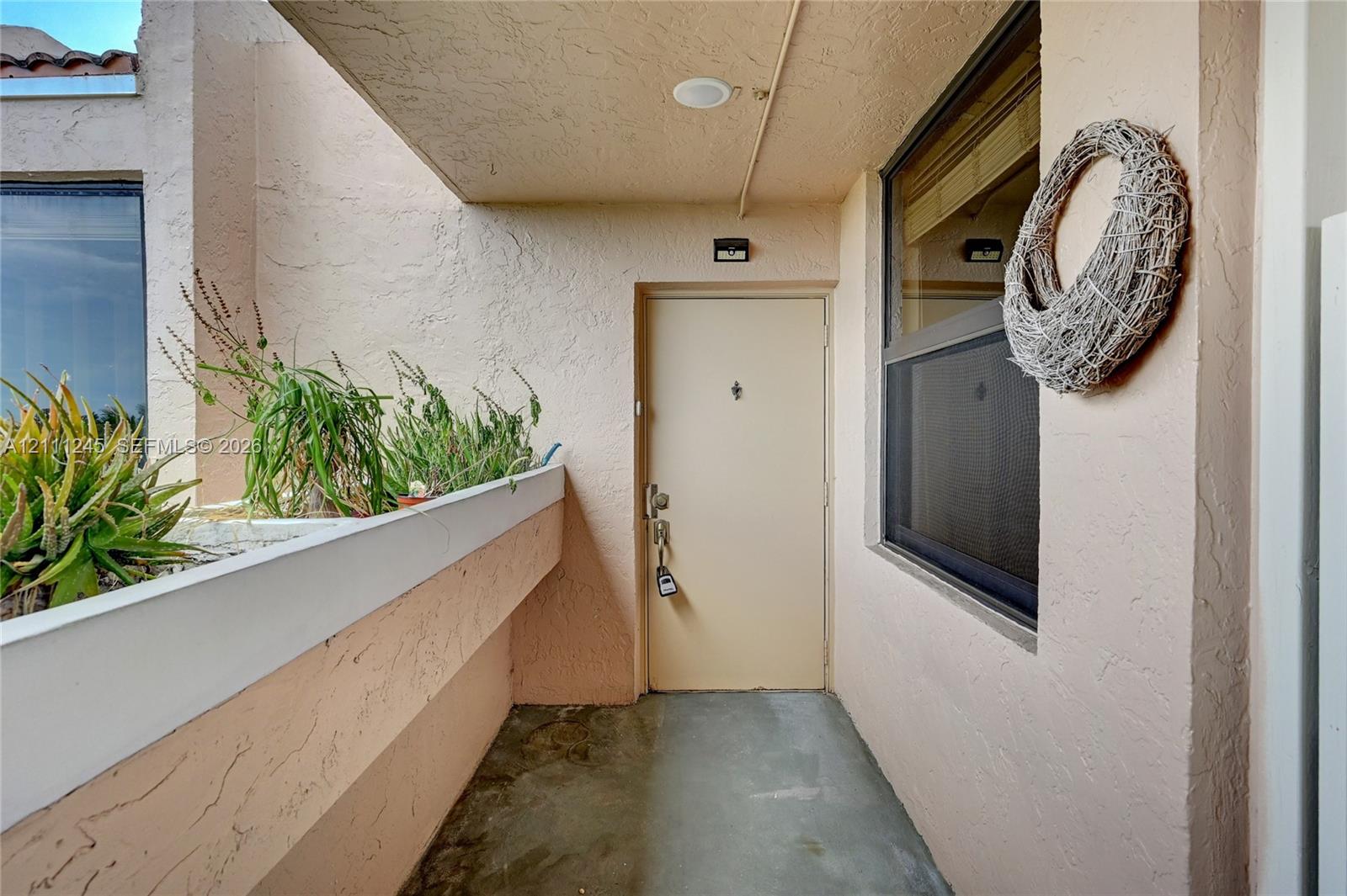 Covered entryway featuring textured stucco walls, a concrete floor, integrated recessed lighting, and a built-in stucco planter Covered entryway featuring textured stucco walls, a concrete floor, integrated recessed lighting, and a built-in stucco planter