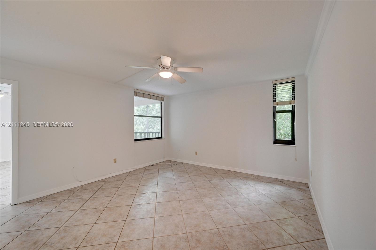 Interior space featuring neutral-toned tile flooring, white wall finishes, a central ceiling fan with integrated lighting, and multiple windows with fixed treatments