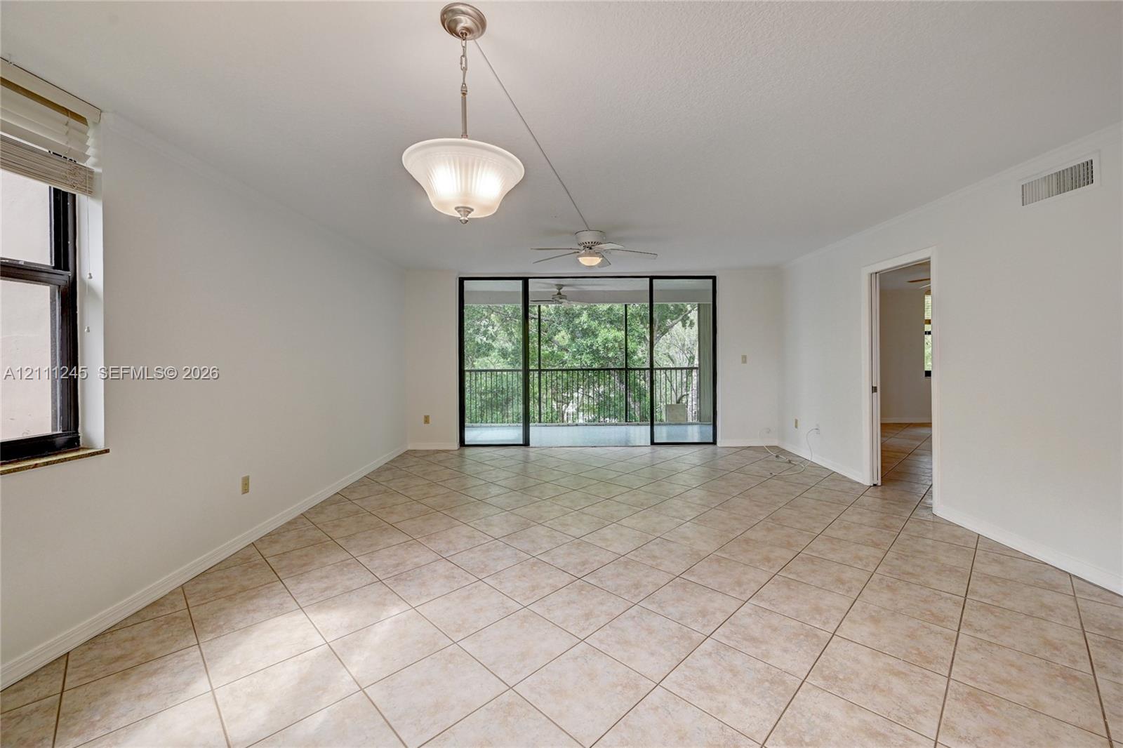 Open-concept interior featuring large-format diagonal tile flooring, a dual-light hanging pendant fixture, a ceiling fan with integrated lighting, and floor-to-ceiling sliding glass doors opening to a screened balcony