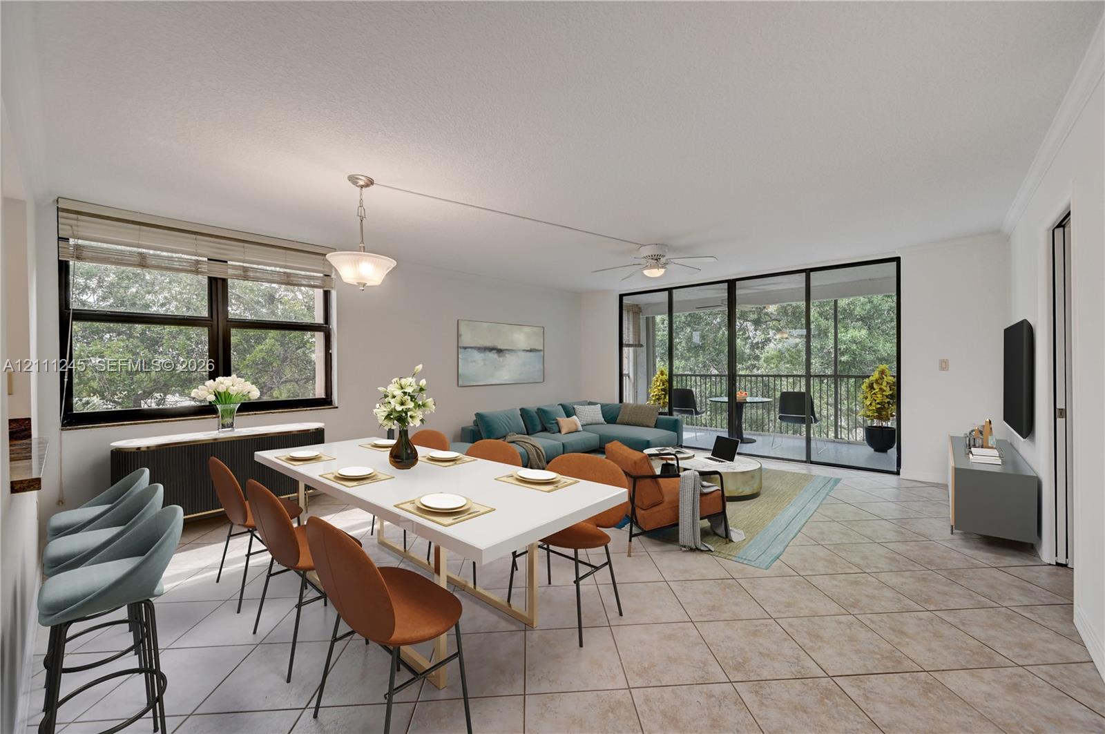 Open-concept living space featuring diagonal-set tile flooring, multi-panel sliding glass doors to the balcony, recessed crown molding, and a ceiling fan with integrated lighting