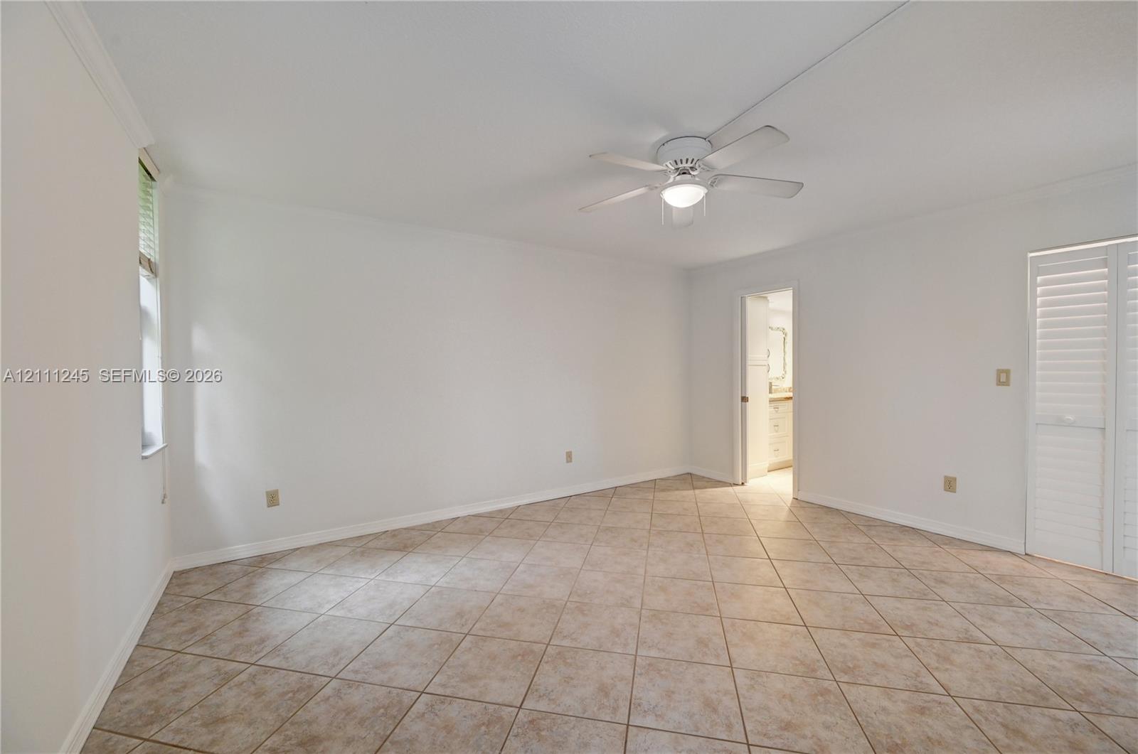 Neutral-toned tile flooring, ceiling fan with integrated lighting, and white plantation-style shutters