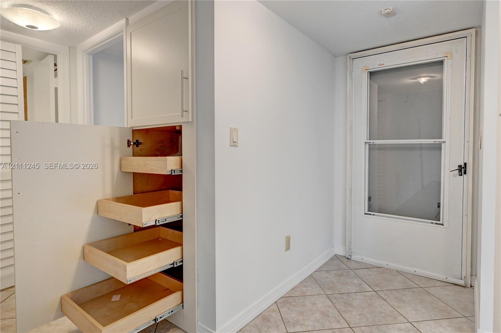 Built-in floor-to-ceiling cabinetry featuring pull-out wooden drawers, ceramic tile flooring, and a glass-paneled exterior door