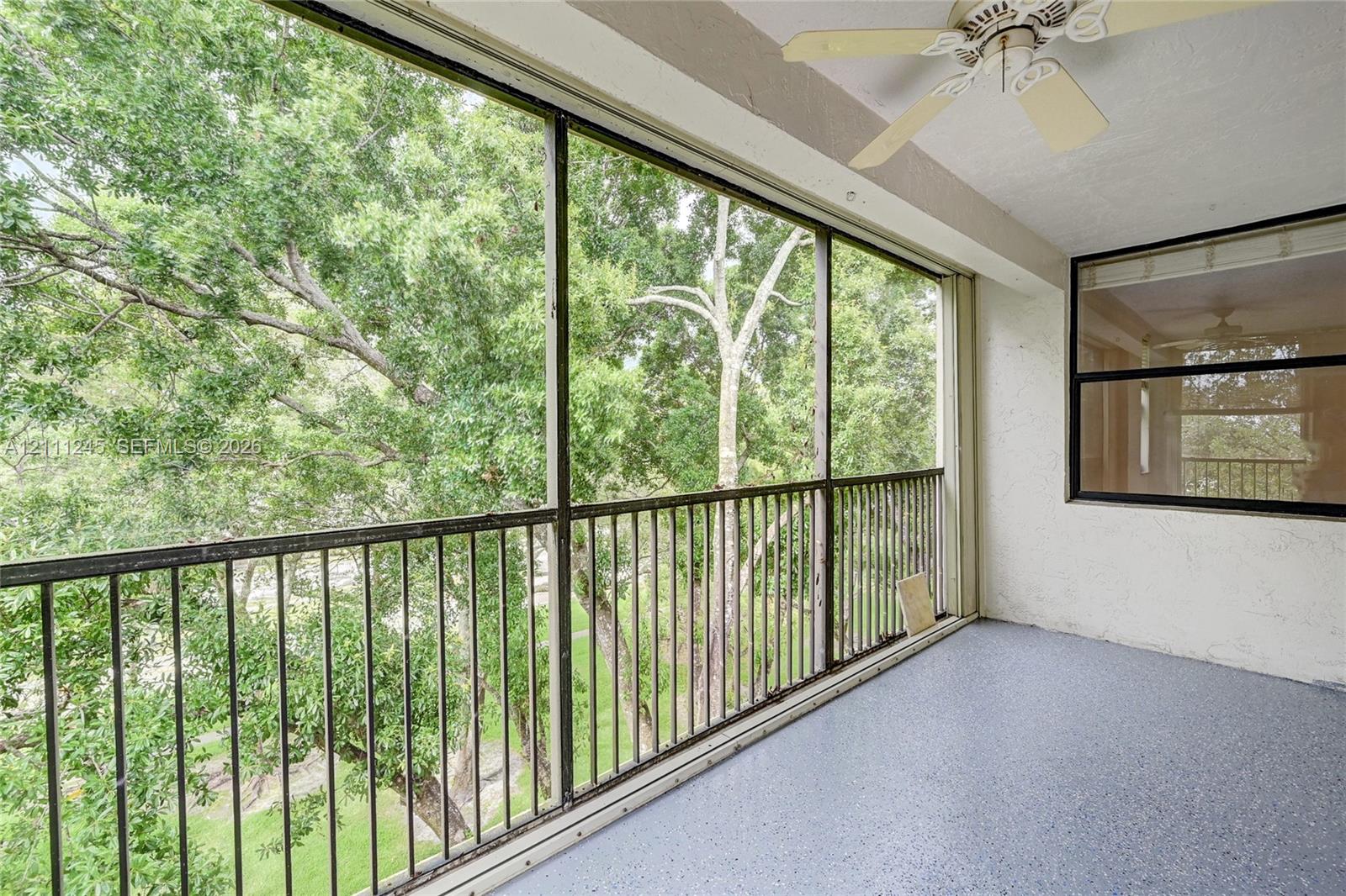 Screened-in balcony featuring metal railings, textured concrete flooring, and a ceiling-mounted fan