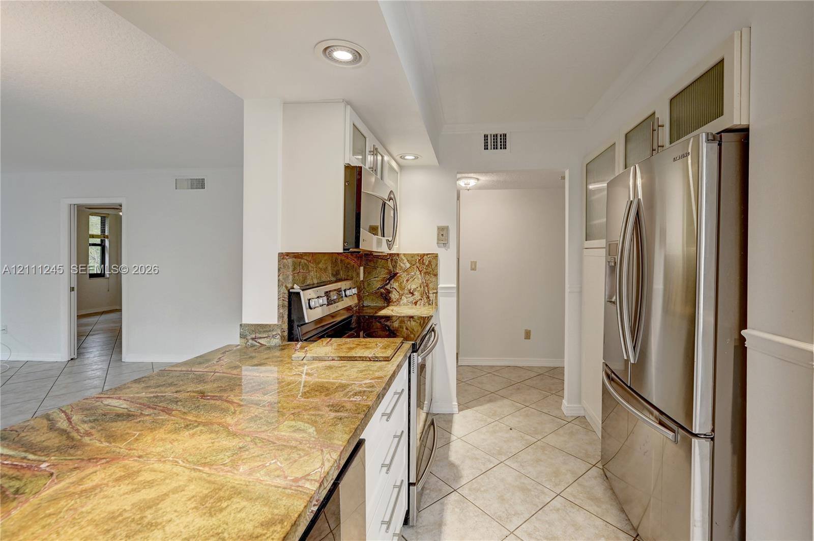Kitchen featuring stone countertops, white cabinetry with glass-panel upper doors, stainless steel refrigerator, built-in microwave, and tile flooring