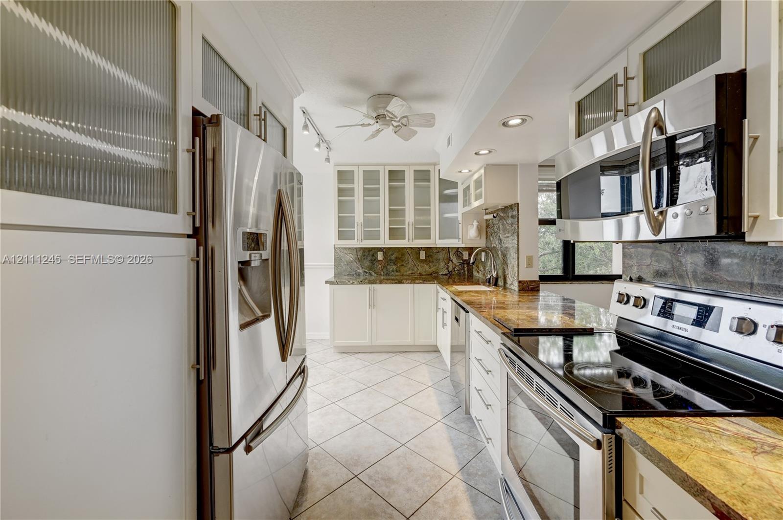 Kitchen featuring white cabinetry with glass-panel upper doors, stainless steel appliances, stone countertops, tiled backsplash, and stone-tile flooring