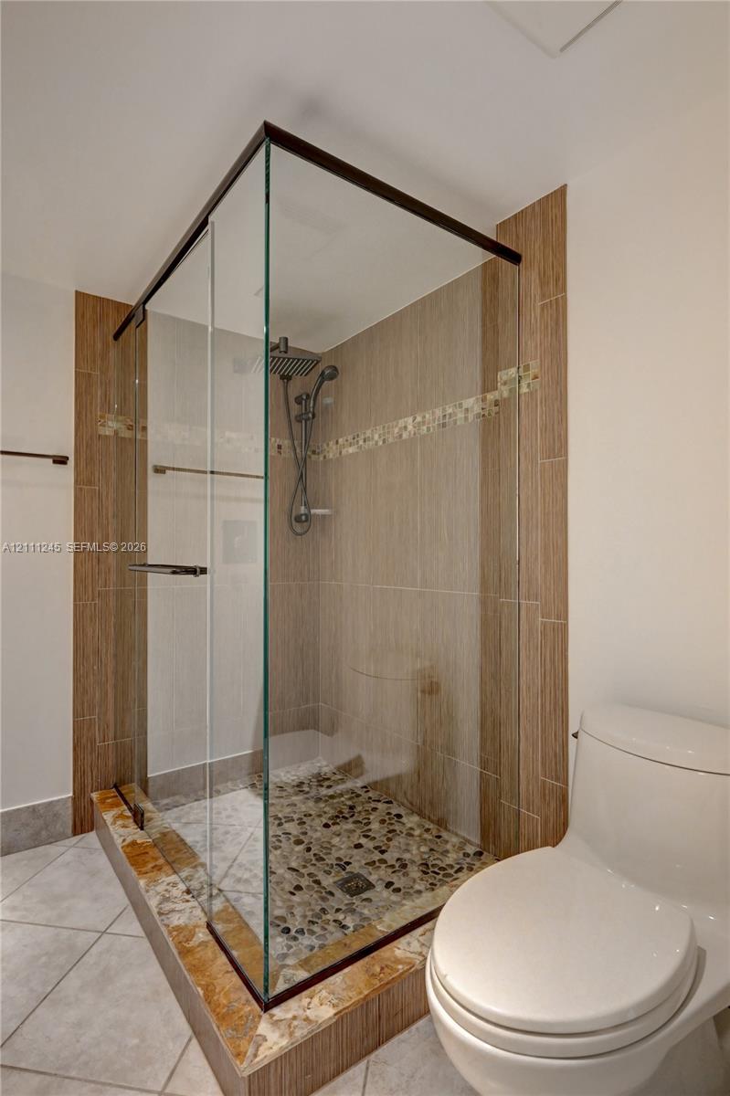 Walk-in glass-enclosed shower featuring a river rock floor, multi-head shower system, decorative tile accents, and stone-tiled shower curb