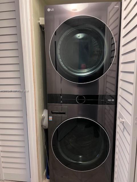 Stackable laundry unit featuring a sleek black finish, glass-front doors, and louvered closet doors