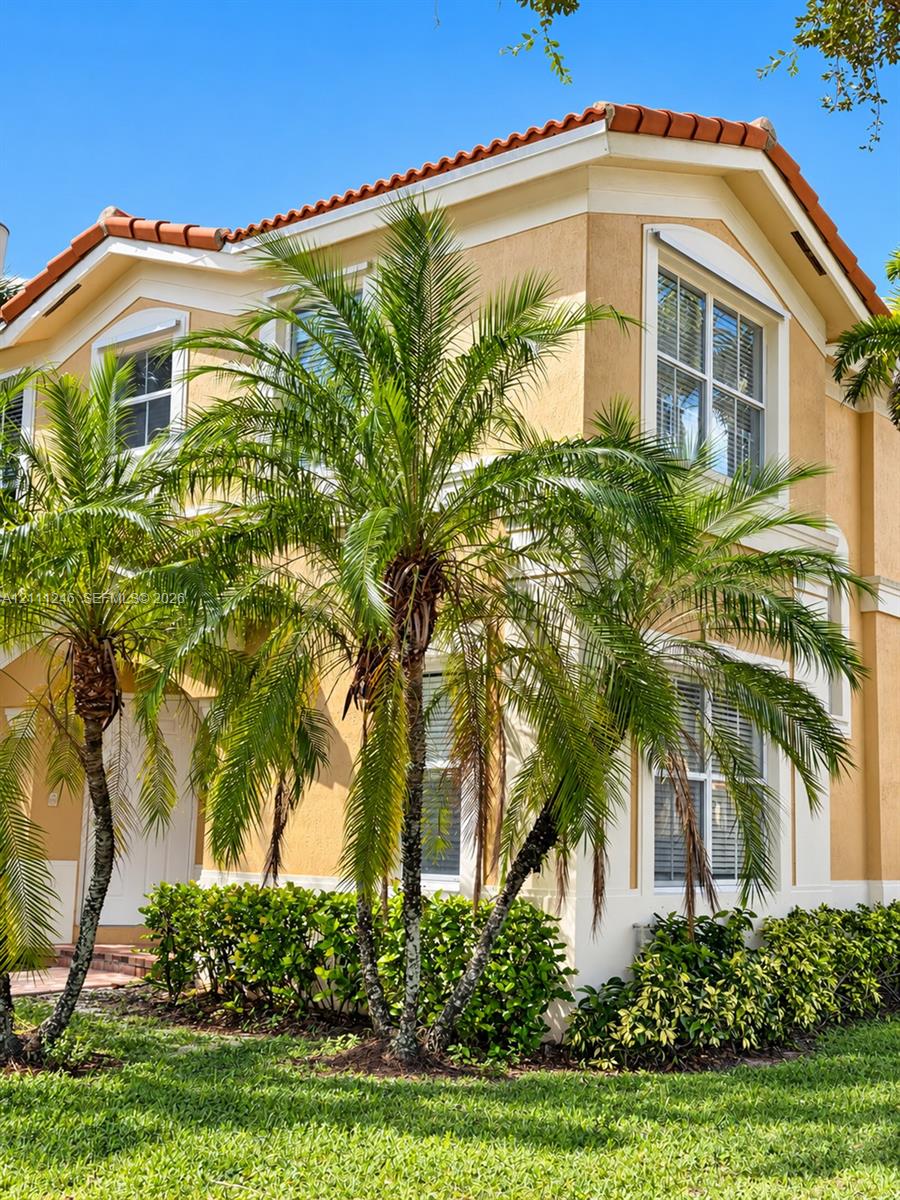 Stucco exterior featuring a multi-gabled terracotta tile roof, white trim accents, and mature palm tree landscaping Stucco exterior featuring a multi-gabled terracotta tile roof, white trim accents, and mature palm tree landscaping