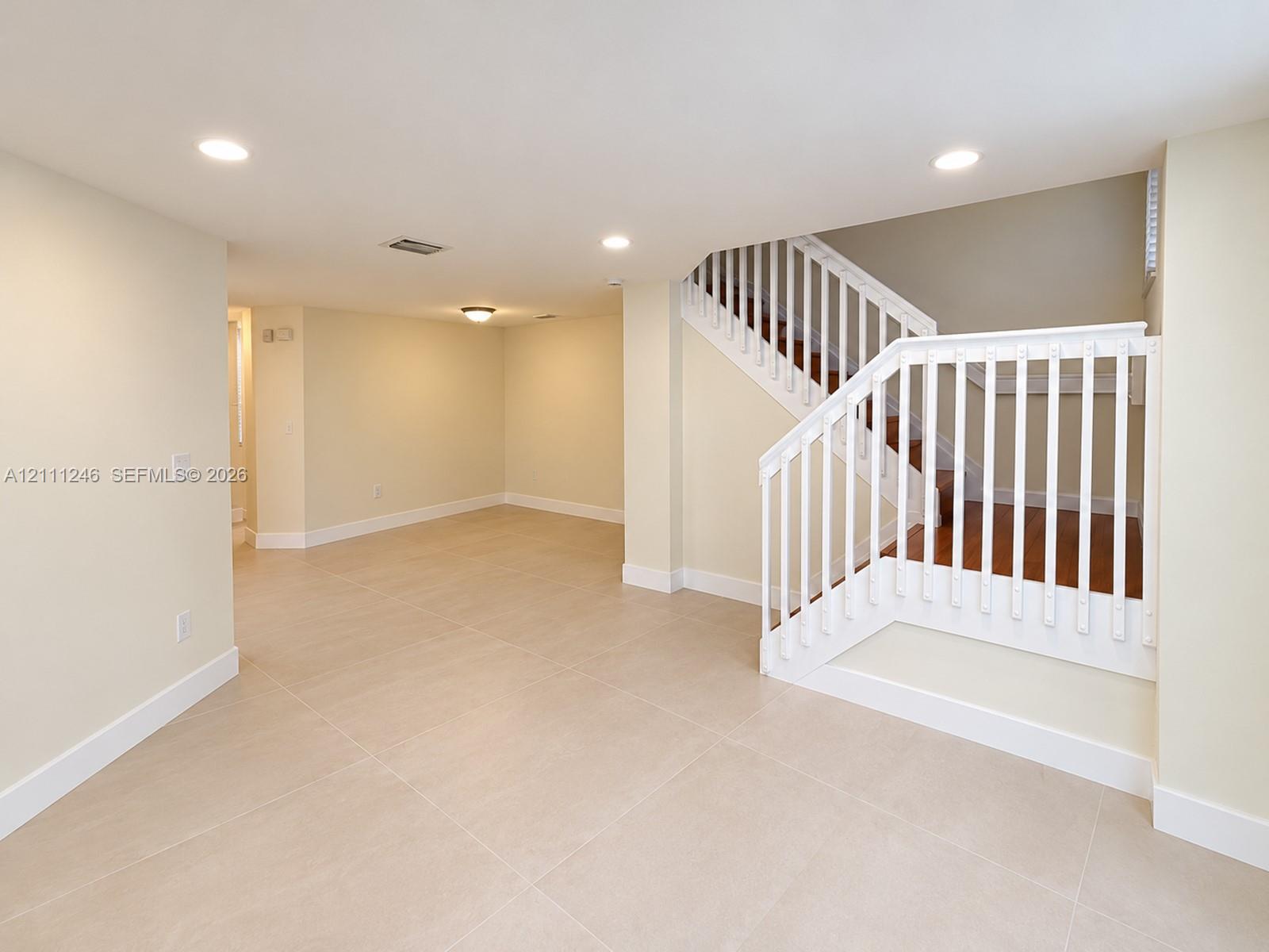 Open-concept interior featuring large-format tile flooring, recessed lighting, and a staircase with white balusters and wood-finish treads