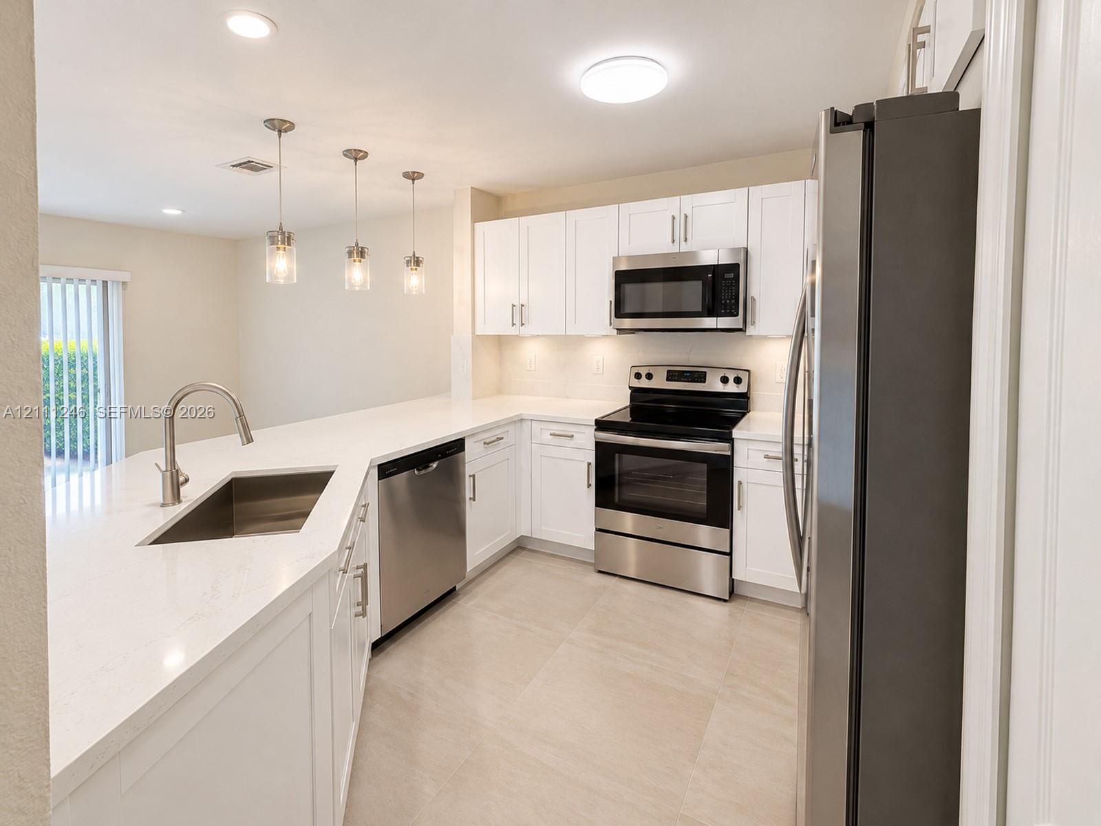 Kitchen featuring white shaker-style cabinetry, solid-surface countertops, stainless steel appliances, a peninsula with an undermount sink, and light-toned tile flooring Kitchen featuring white shaker-style cabinetry, solid-surface countertops, stainless steel appliances, a peninsula with an undermount sink, and light-toned tile flooring
