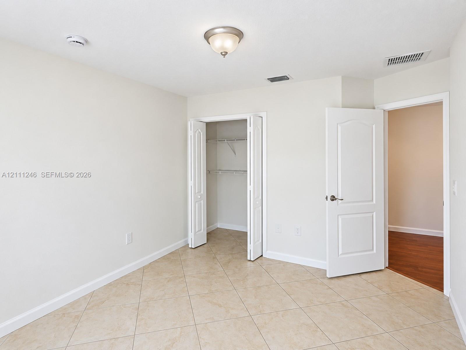 Neutral-toned tile flooring, bi-fold closet doors, and interior arched-panel door with brushed nickel hardware