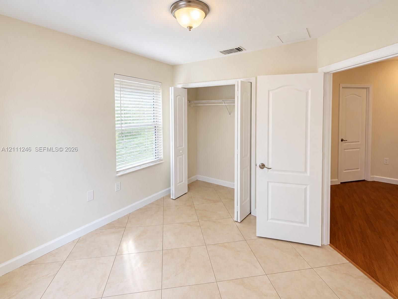 Neutral-toned ceramic tile flooring, walk-in closet with built-in shelving, multi-panel interior doors, and window with adjustable blinds