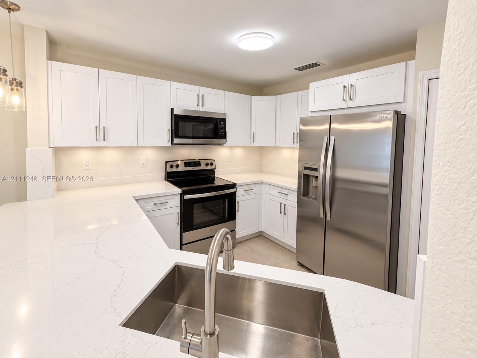 Kitchen featuring white shaker-style cabinetry, white countertops with grey veining, stainless steel appliances, and an undermount stainless steel sink with a high-arch faucet Kitchen featuring white shaker-style cabinetry, white countertops with grey veining, stainless steel appliances, and an undermount stainless steel sink with a high-arch faucet