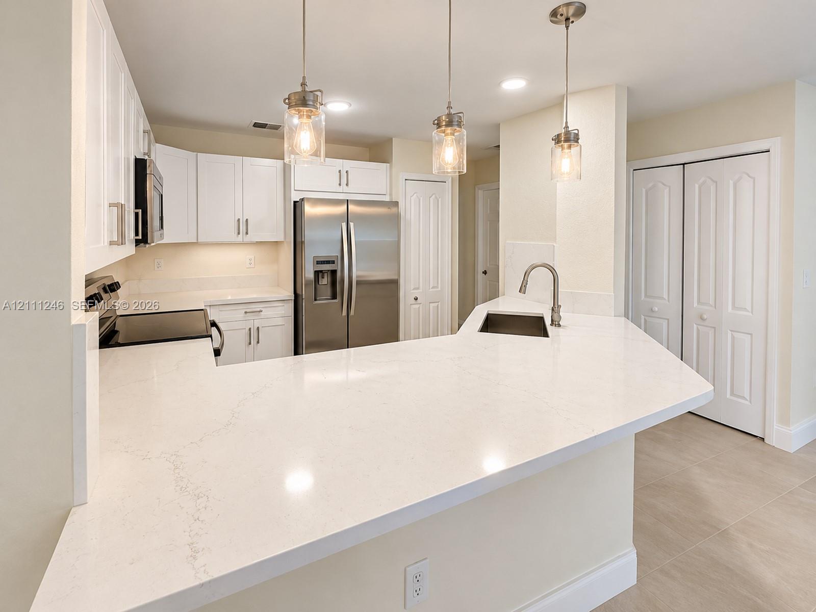 Kitchen featuring white cabinetry, quartz countertops, stainless steel appliances, a peninsula with an undermount sink, and three glass pendant lights Kitchen featuring white cabinetry, quartz countertops, stainless steel appliances, a peninsula with an undermount sink, and three glass pendant lights