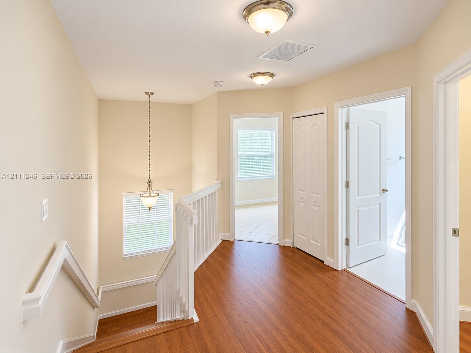 Interior landing featuring wood-finish flooring, white spindle balusters, multi-panel doors, and overhead globe lighting fixtures