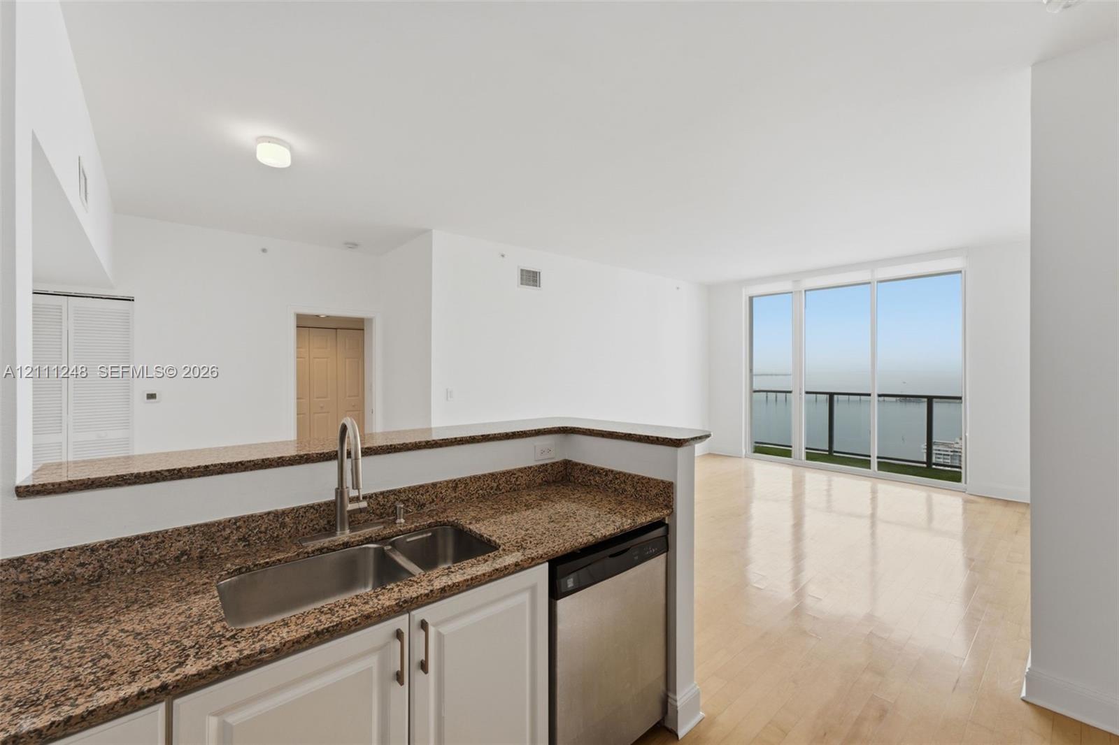 Kitchen featuring stone-finish countertops, stainless steel dual-basin sink, wood-finish flooring, and floor-to-ceiling glass panel windows
