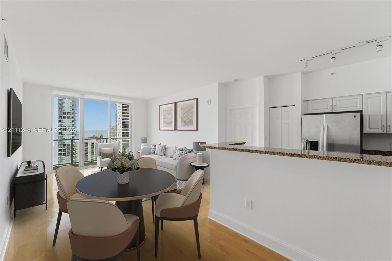 Open-concept living space featuring wood-finish flooring, floor-to-ceiling windows, and a kitchen peninsula with a stone-finish countertop