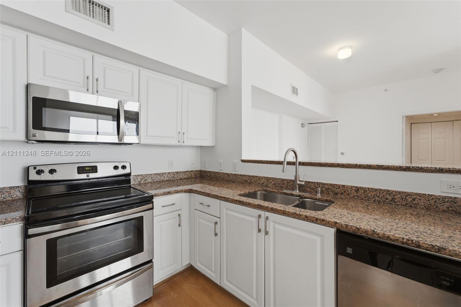 Kitchen featuring white cabinetry, stone-finish countertops, stainless steel appliances, double-basin sink with a gooseneck faucet, and wood-finish flooring