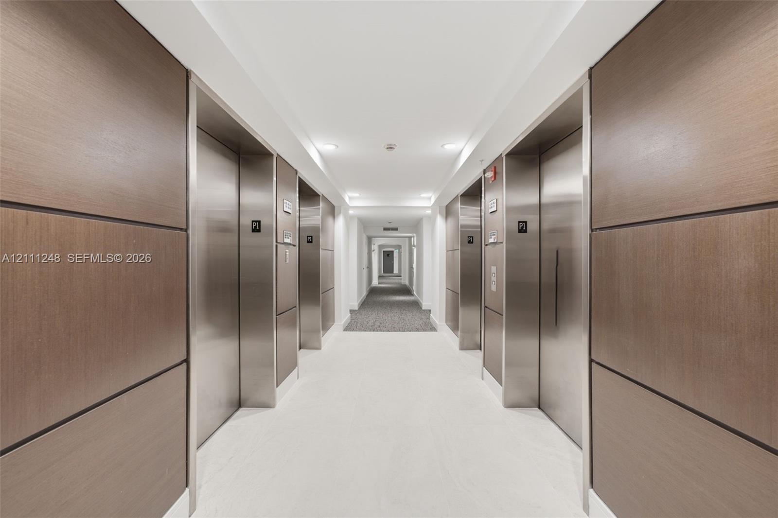 Elevator lobby featuring metallic doors, wood-paneled walls, and recessed ceiling lighting