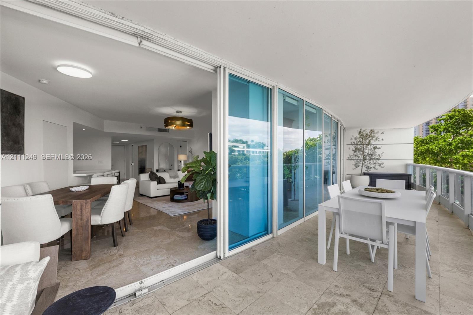 Covered balcony with natural stone flooring, expansive glass sliding door system, and metal railing