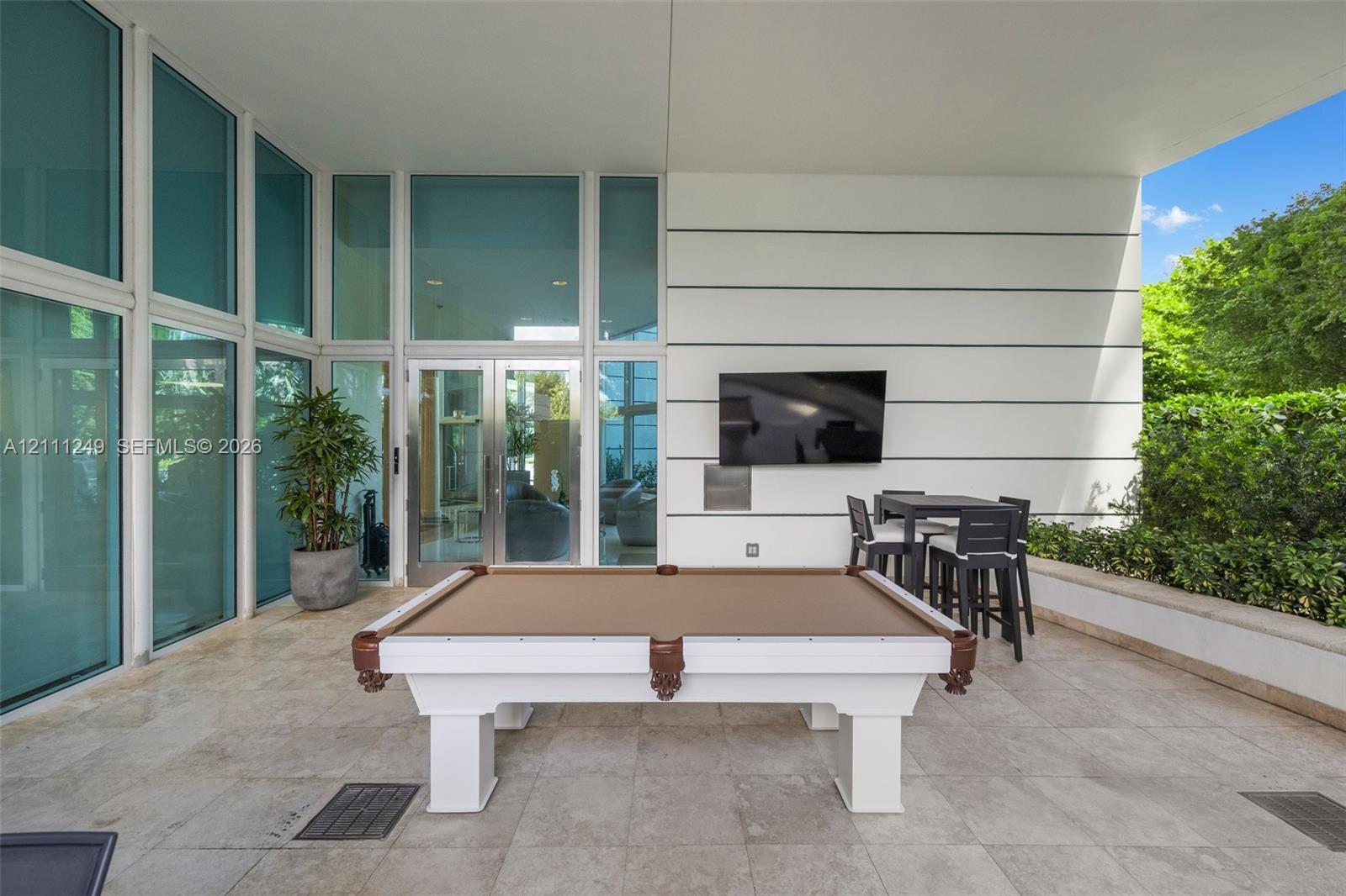 Covered patio featuring large-format stone tile flooring, expansive glass wall panels, and horizontally paneled exterior siding