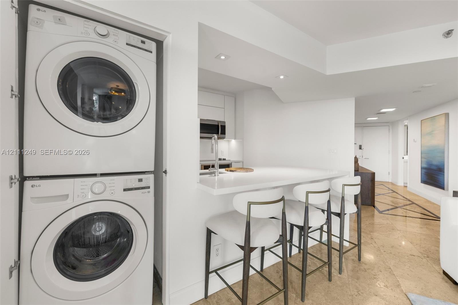 Stacked laundry unit featuring a white front-load washer and dryer, stone-surface breakfast bar with integrated sink, and stone tile flooring