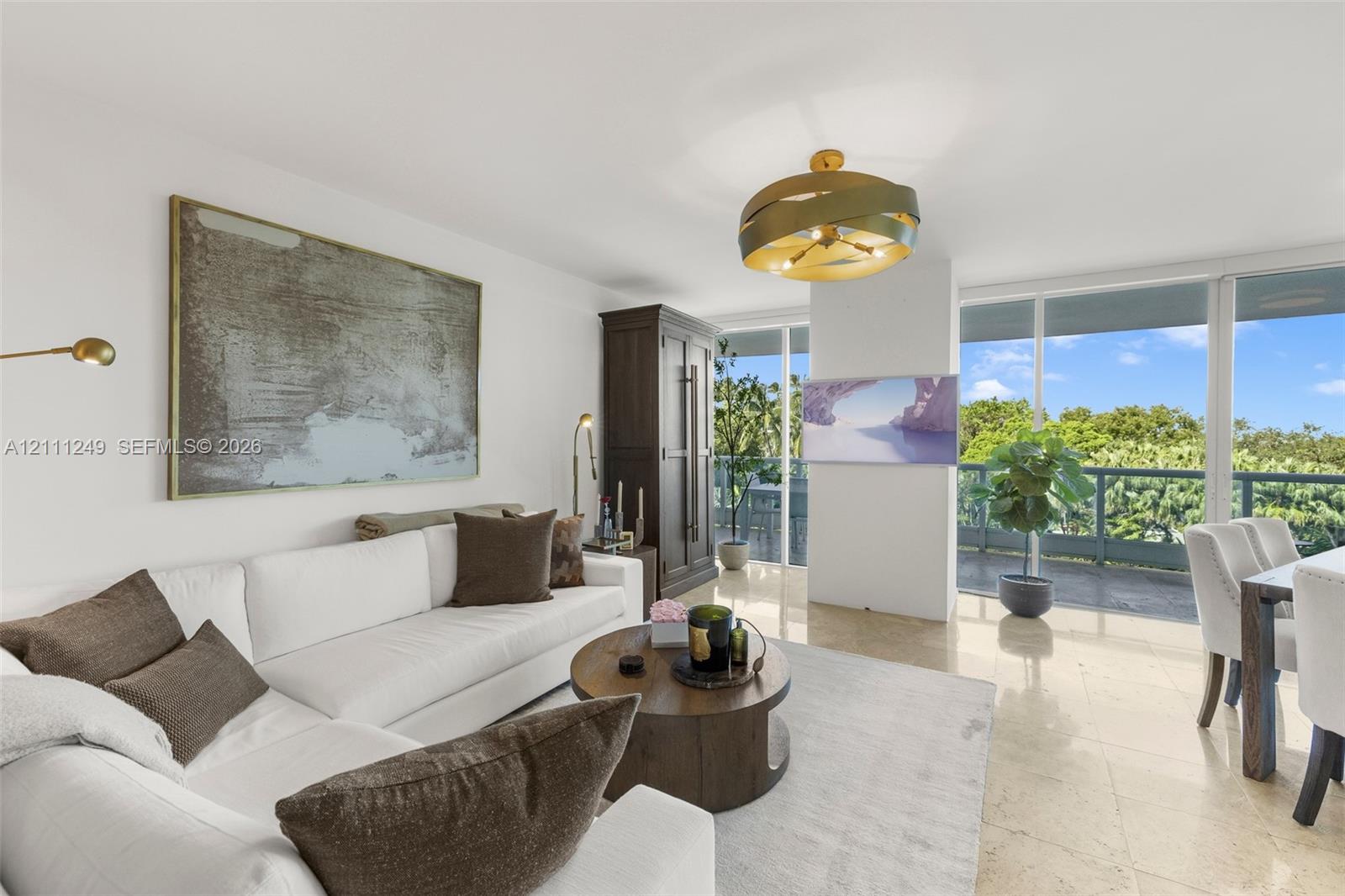 Living area featuring large-format stone flooring, floor-to-ceiling glass windows, a brass-finish contemporary chandelier, and a private balcony with natural scenery Living area featuring large-format stone flooring, floor-to-ceiling glass windows, a brass-finish contemporary chandelier, and a private balcony with natural scenery