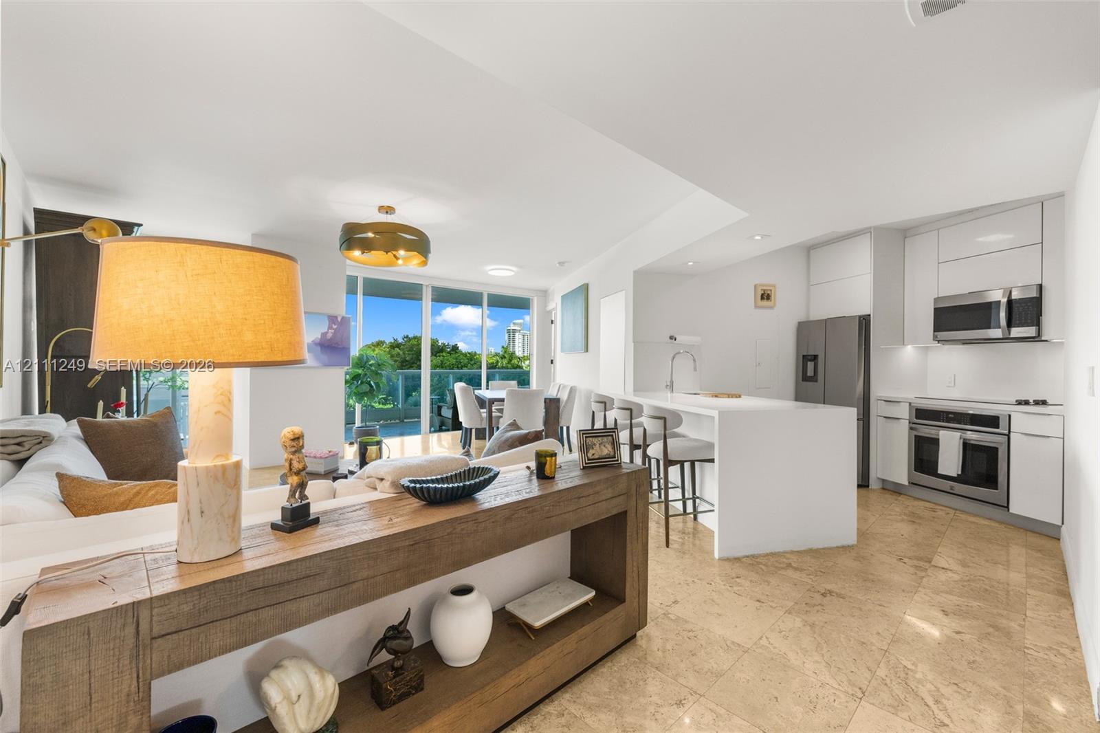 Open concept interior featuring stone-tile flooring, sleek white flat-panel cabinetry, a stainless steel appliance suite, and a waterfall-edge kitchen island Open concept interior featuring stone-tile flooring, sleek white flat-panel cabinetry, a stainless steel appliance suite, and a waterfall-edge kitchen island