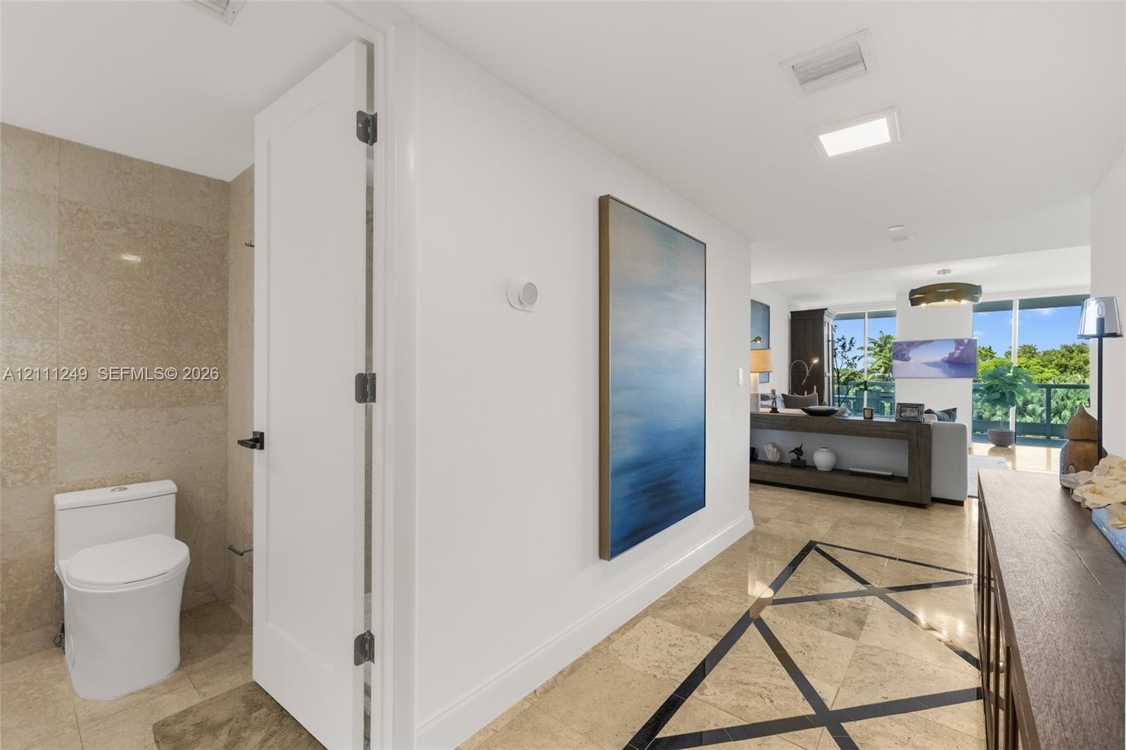 Bathroom featuring a white integrated countertop and basin, high-gloss flat-panel cabinetry, large-format neutral wall tile, wall-to-wall mirror, and recessed ceiling lighting Bathroom featuring a white integrated countertop and basin, high-gloss flat-panel cabinetry, large-format neutral wall tile, wall-to-wall mirror, and recessed ceiling lighting