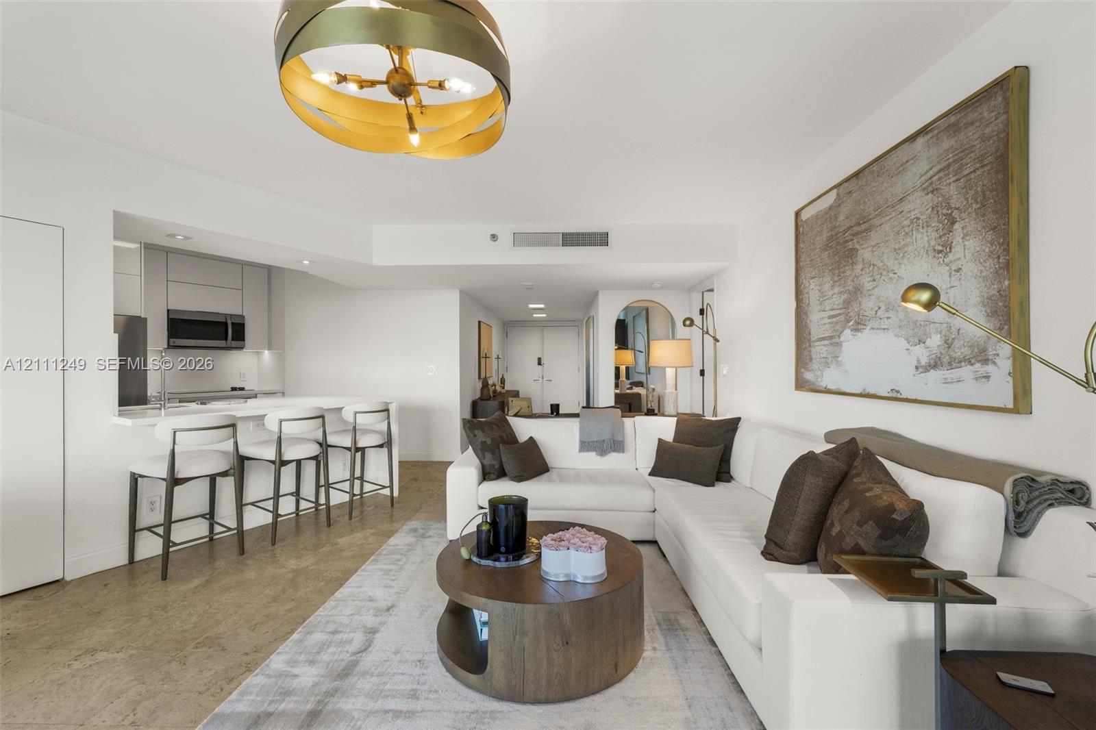 Open-concept living space featuring high-gloss cabinetry, a quartz waterfall-edge breakfast bar, polished concrete flooring, and a contemporary multi-tiered orb pendant light fixture Open-concept living space featuring high-gloss cabinetry, a quartz waterfall-edge breakfast bar, polished concrete flooring, and a contemporary multi-tiered orb pendant light fixture