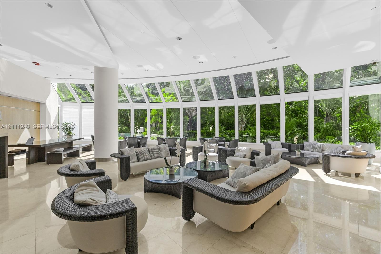 Expansive floor-to-ceiling curved glass wall, polished tile flooring, soaring ceiling with recessed lighting, and a prominent structural column