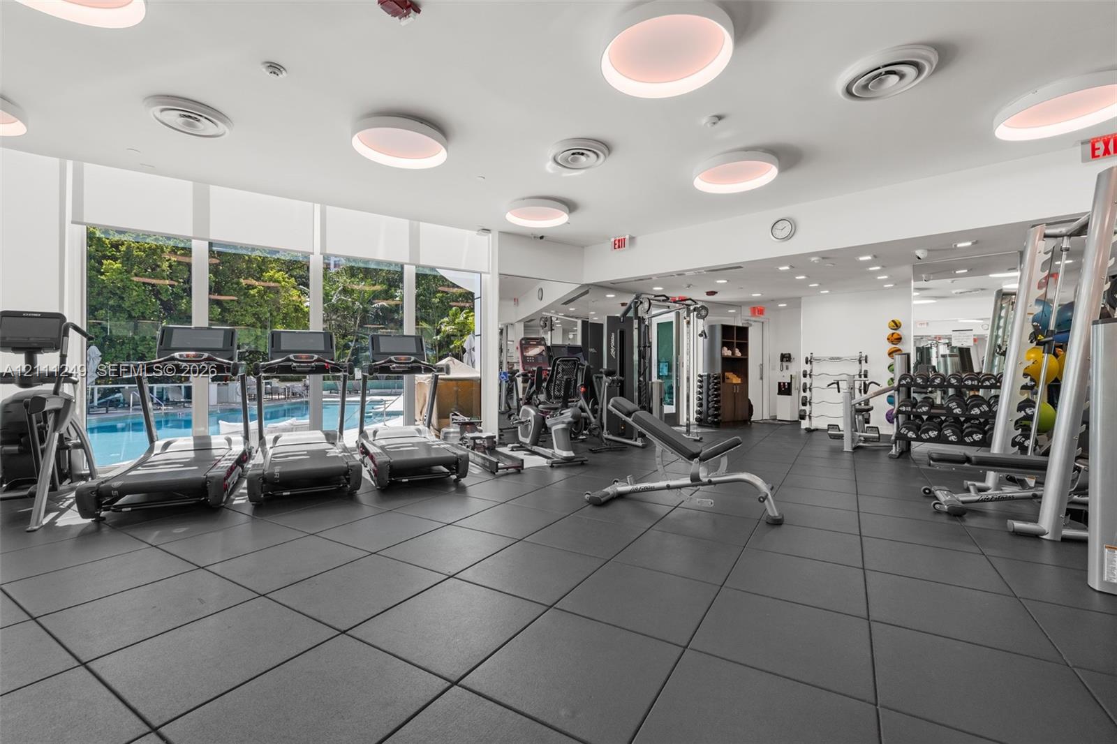 Fitness center featuring floor-to-ceiling windows, rubberized flooring, flush-mount circular lighting, and integrated wall mirrors