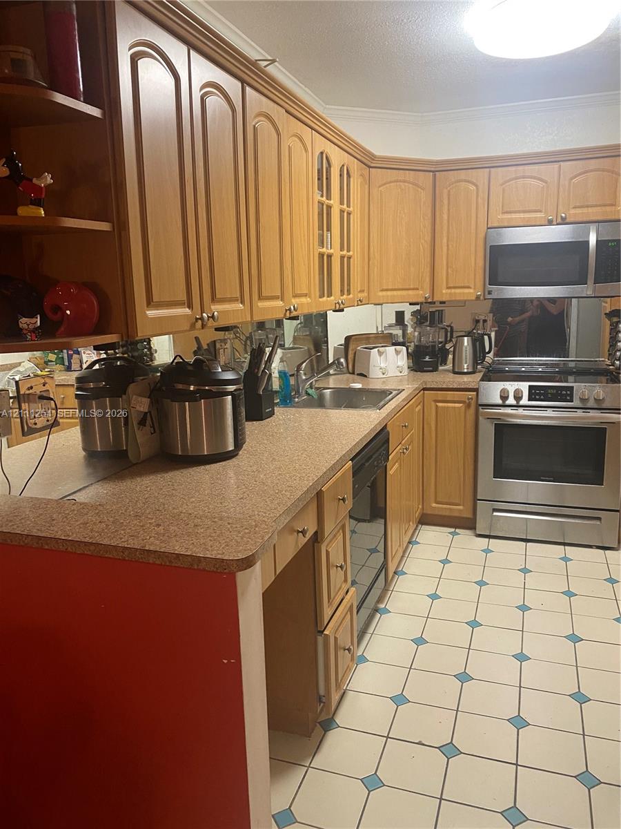 Kitchen featuring light-tone wood cabinetry, stone-composite countertops, stainless steel appliances, and tile flooring with decorative inlay accents