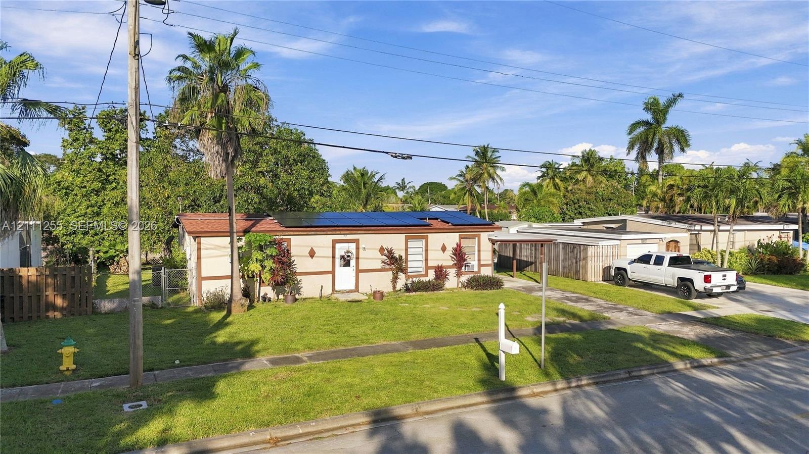 Single-story exterior featuring rooftop solar panels, a covered carport, and a manicured lawn with mature palms