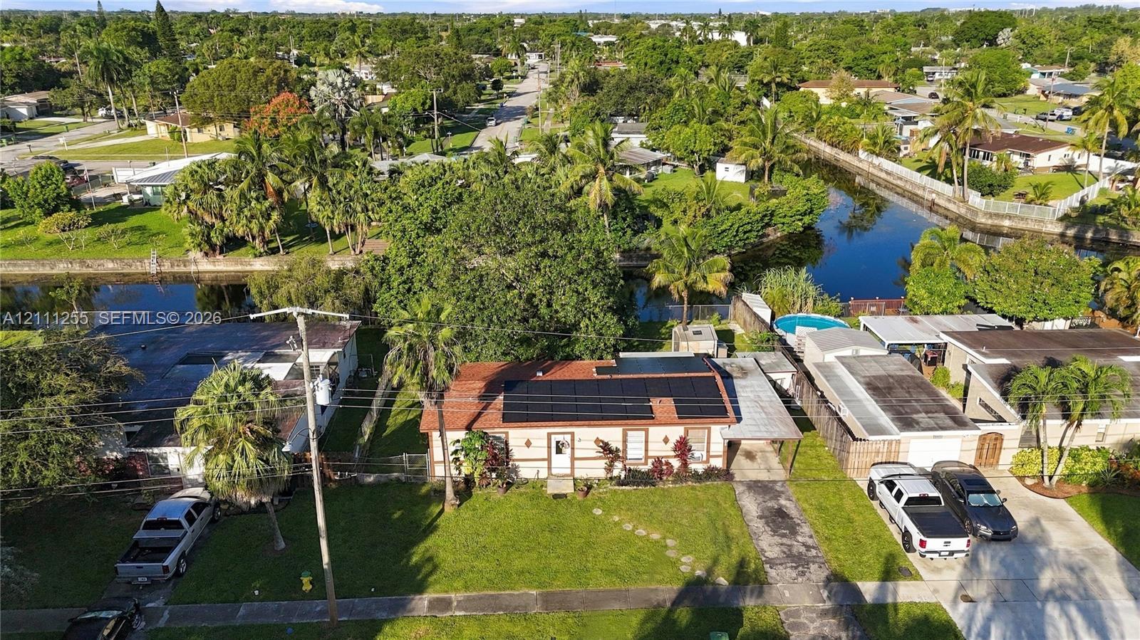 Single-story residence featuring a tile roof, roof-mounted solar panels, attached carport, and canal-front lot with mature landscaping