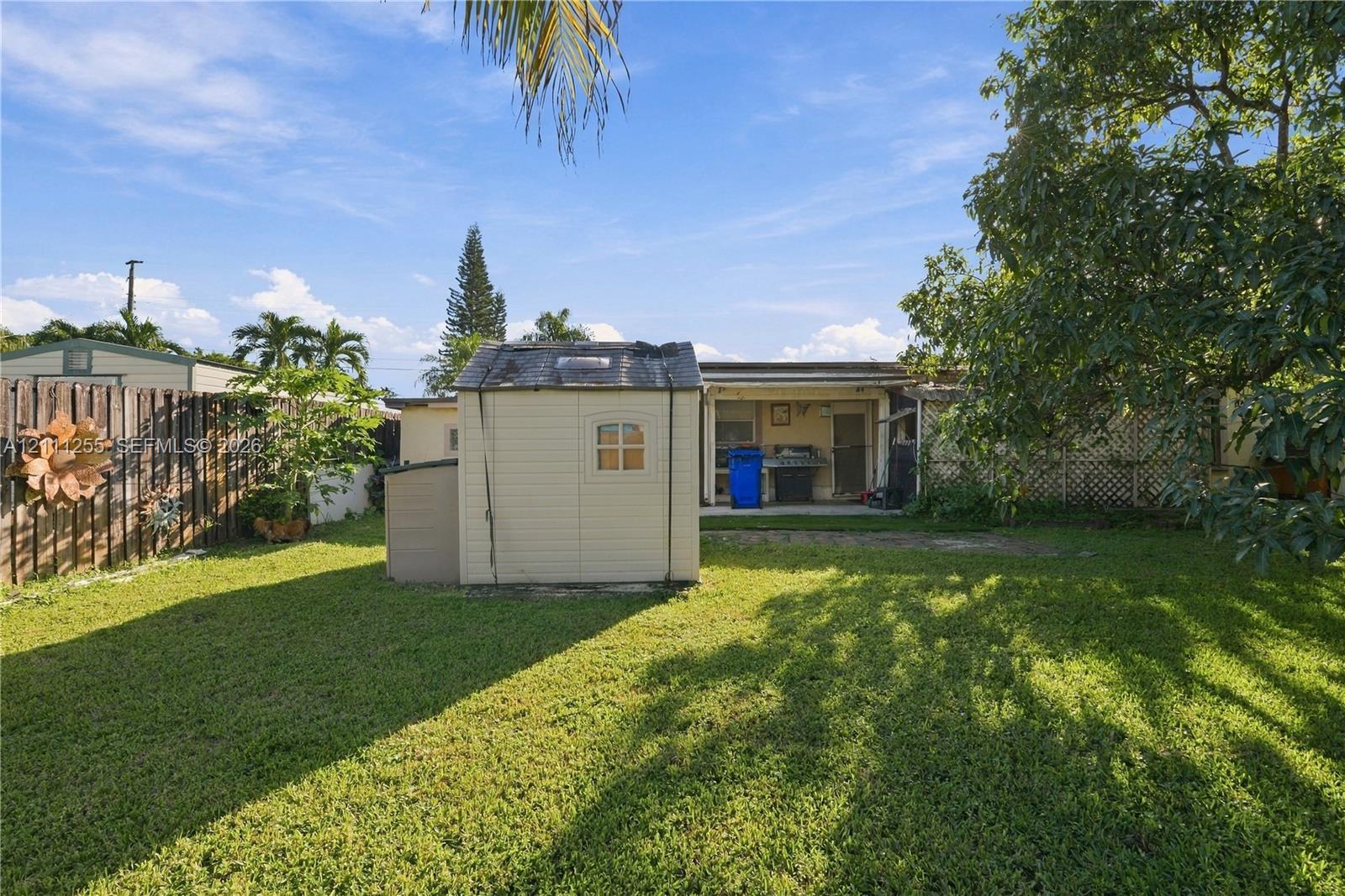 Backyard featuring a grass lawn, wood-panel fencing, mature trees, and a detached exterior storage structure